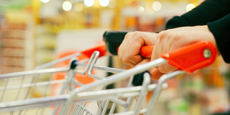 Mãos empurrando um carrinho de supermercado, ilustrando a imagem sobre economizar no mercado.