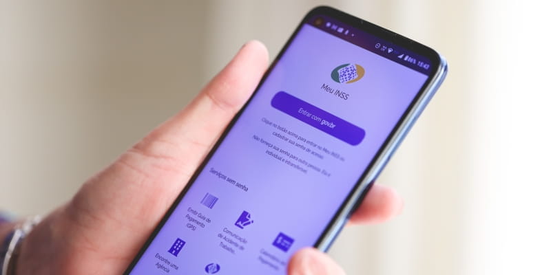 Uma pessoa segurando um celular com o aplicativo Meu INSS, ilustrando a matéria sobre o anúncio do INSS fechado.