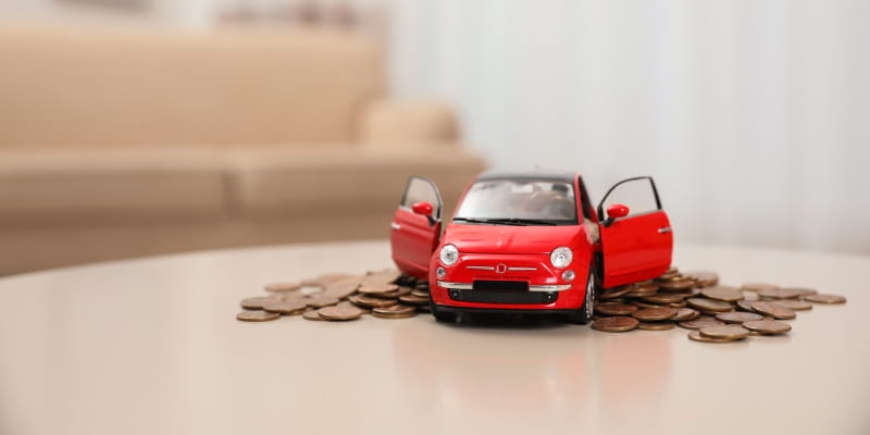 Uma miniatura de carro sobre moedas em cima de uma mesa, ilustrando a matéria sobre o IPVA 2026 no Centro-oeste.