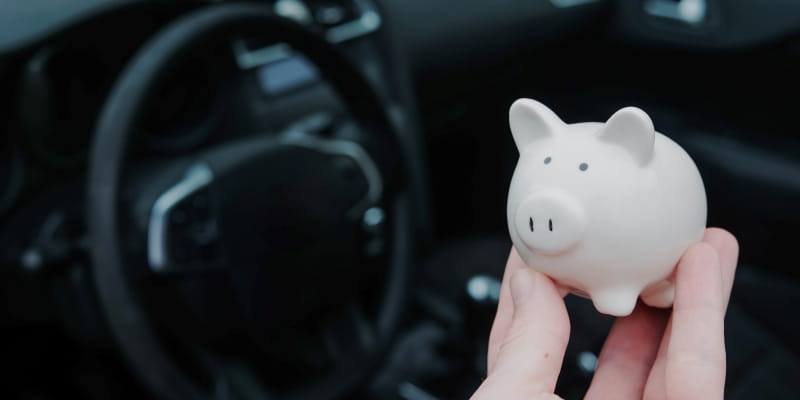 Uma mão segurando um cofrinho de porco dentro de um carro para ilustrar a matéria sobre o IPVA 2026 no Sul.