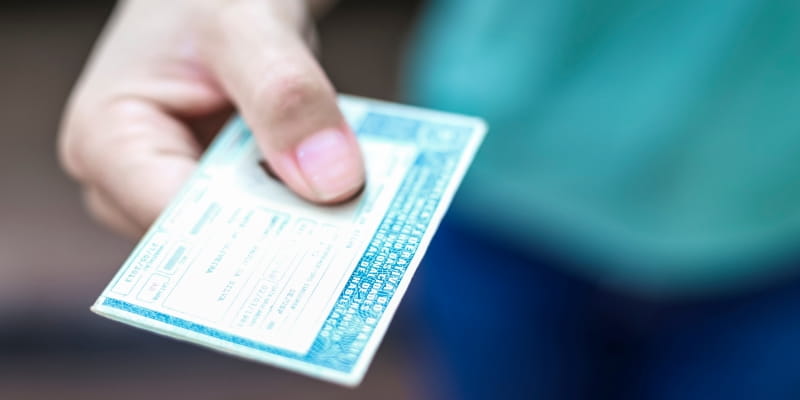 Uma mão masculina mostrando uma  Carteira Nacional de Motorista (CNH), ilustrando a matéria sobre as mudanças na CNH.