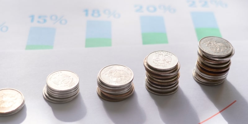 Moedas no fundo de um gráfico com percentagens. Imagem para ilustrar a matéria sobre taxa de juros em 2026.