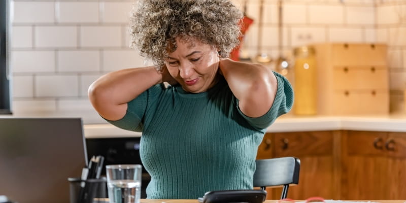 Uma mulher sentada em uma cadeira, com as mãos no pescoço, demonstrando sobrecarga ao ter pouco tempo livre.