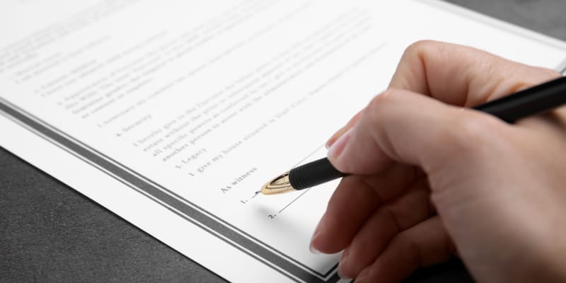 Mãos de uma pessoa assinando um testamento.