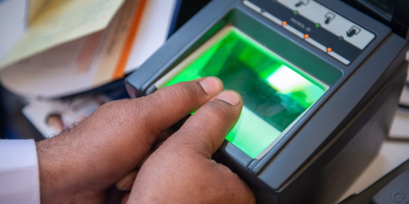 Mãos masculinas fazendo a biometria do INSS em um aparelho de leitura de digital.