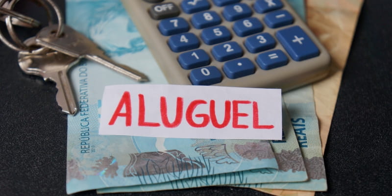 Um papel escrito "aluguel" sobre notas de dinheiro ao lado de uma calculadora e chaves, ilustrando a matéria sobre o preço do aluguel residencial.