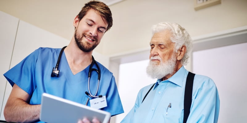 Enfermeiro com tablet em consulta para diagnóstico médico orientando um paciente idoso sobre prevenção.