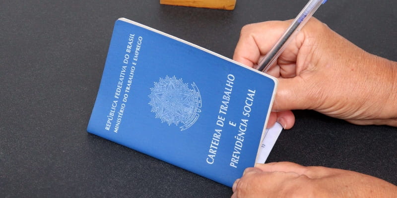 Mãos de uma pessoa assinando uma carteira de trabalho para ilustrar a matéria sobre tempo de contriuição do INSS.