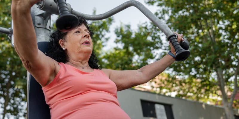 Uma mulher idosa acima do peso fazendo musculação em um parque ao ar livre.