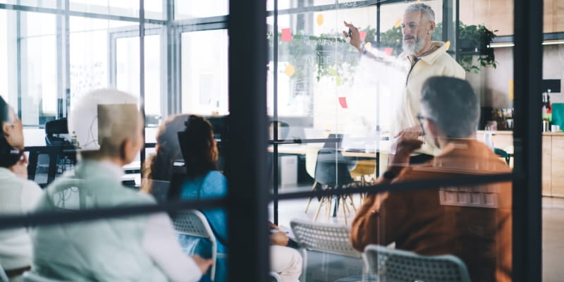 Um CEO fundador de sucesso, com ar orgulhoso, explica a estratégia a uma equipa de profissionais durante uma sessão de brainstorming no interior do escritório.