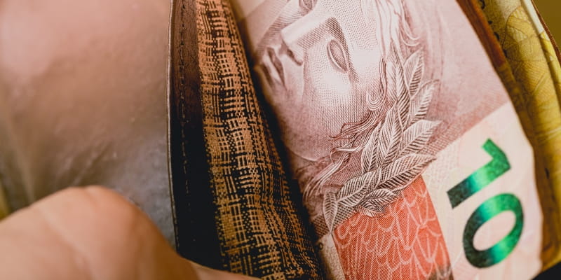 Uma mão abrindo uma carteira que tem 10 reais e algumas notas, ilustrando o baixo poder de compra em meio a alta de preços.