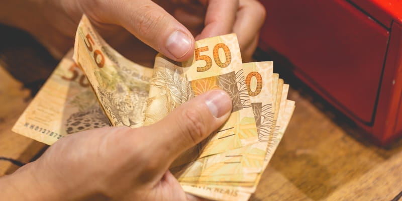 Mãos de uma pessoa segurando notas de 50 reais, ilustrando a matéria sobre atrasados do INSS.