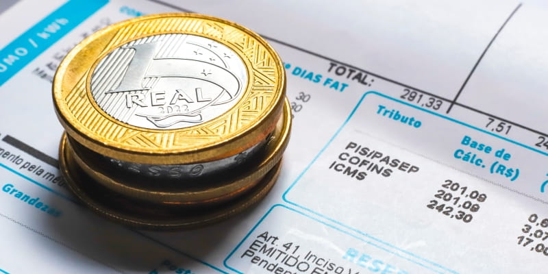 Moedas empilhadas sobre uma conta de luz para ilustrar a matéria sobre como economizar energia elétrica.