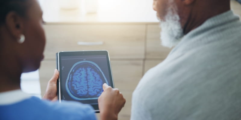 Uma médica mostrando o exame de cérebro para um paciente, ilustrando a matéria sobre exame de sangue para Alzheimer.