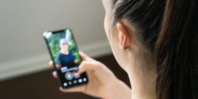 Mulher olhando perfil do homem na tela do telefone ao cair no golpe do falso romance, um dos golpes com inteligência artificial mais comuns em 2026.