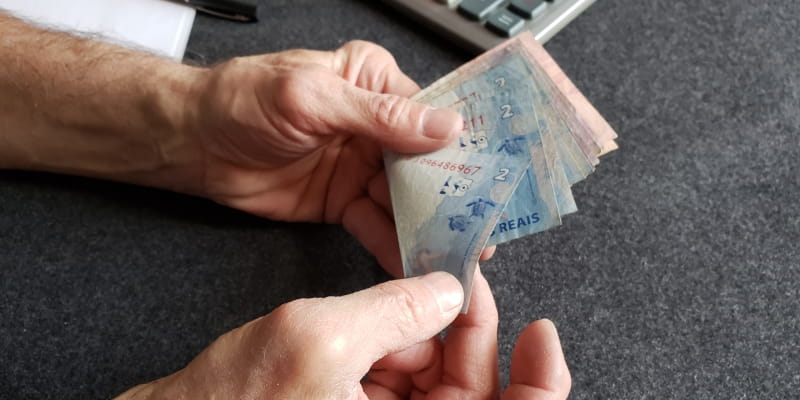 Mãos de uma pessoa idosa contando notas de dinheiro, ilustrando a matéria sobre abandono financeiro de idosos.