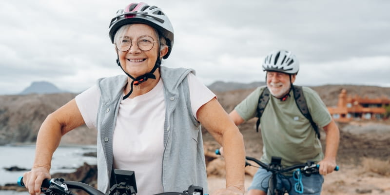 Um casal de idosos praticando ciclismo na terceira idade ao ar livre sorrindo.