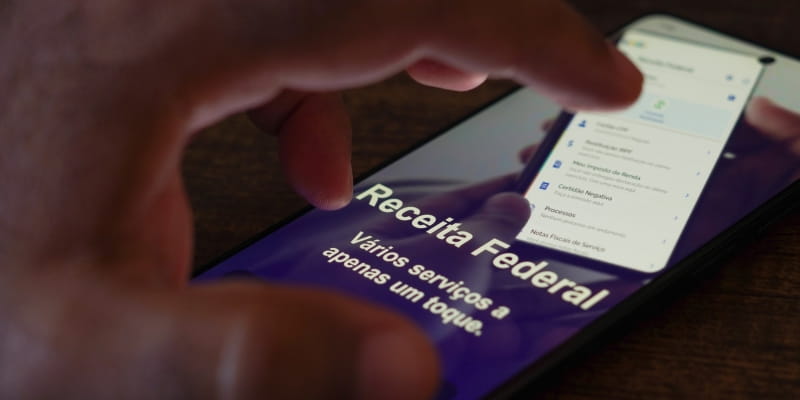 Uma mão tocando em um celular com o aplicativo da receita federal depois de descobrir como declarar plano de saúde no Imposto de Renda.