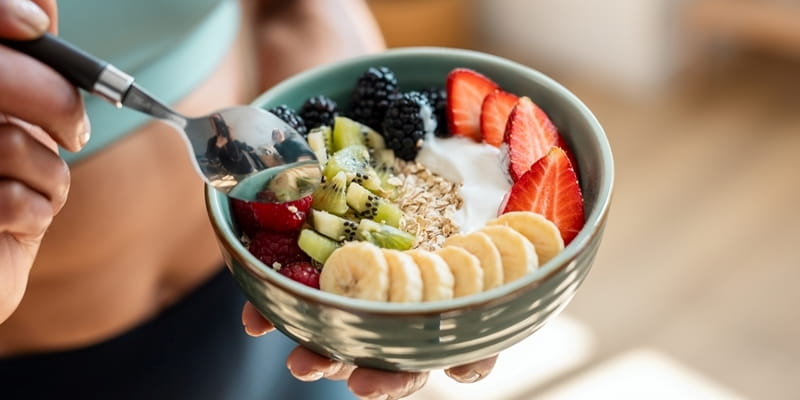 Mãos de uma mulher negra segurando uma tigela de alumínio com iogurte e frutas. Alimentação saudável é um dos hábitos saudáveis para viver melhor.
