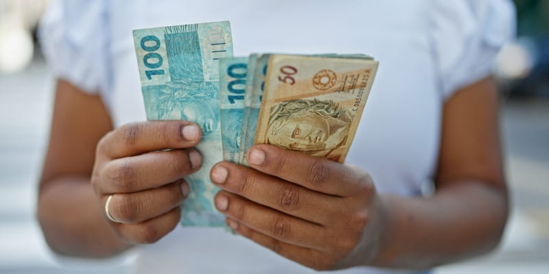 Uma mulher negra segurando notas de dinheiro. Imagem para ilustrar a matéria sobre o Programa de negociação de dívidas do governo.