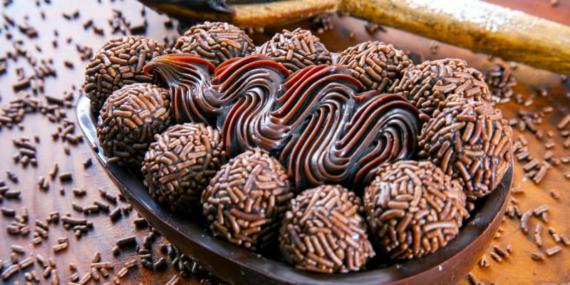 Um ovo de colher com brigadeiros em cima e recheio, ao lado de uma colher de pau também com brigaleiro, ilustrando a matéria sobre renda extra na Páscoa.