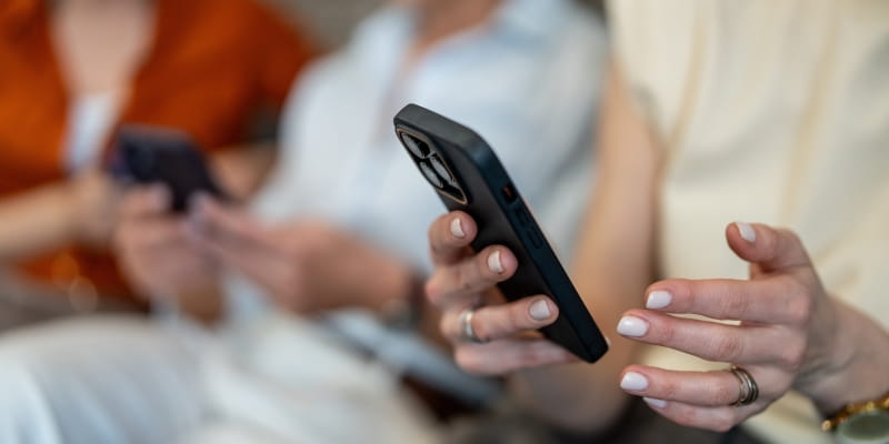 Um grupo de mulheres, cada uma seu celular, consumindo seu tempo de tela de forma passivda. A imagem foca nas mãos das mulheres, cada uma com seu celular;