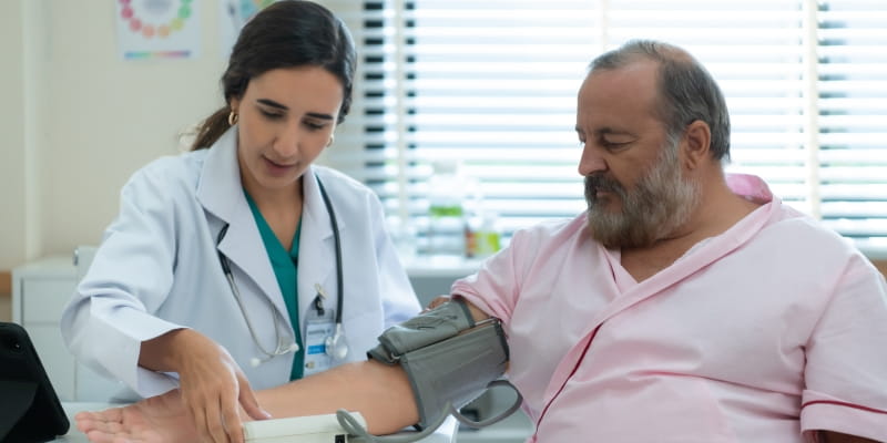 Uma médica fazendo check-up em um homem de cerca de 50 anos. Imagem para ilustrar a matéria sobre exames de rotina por idade.