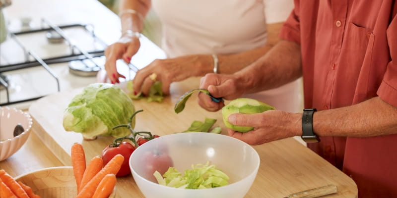 Casal sênior aproveitando o tempo na cozinha, descascando e cortando legumes frescos para uma refeição saudável. Imagem para ilustrar a matéria sobre o segredo dos superidosos.