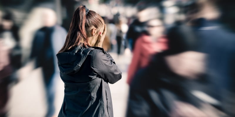 Uma mulher que sofre de transtornos mentais e comportamentais demonstrando estresse ou medo da multidão na rua. Ela está parada e com as mãos no rosto.