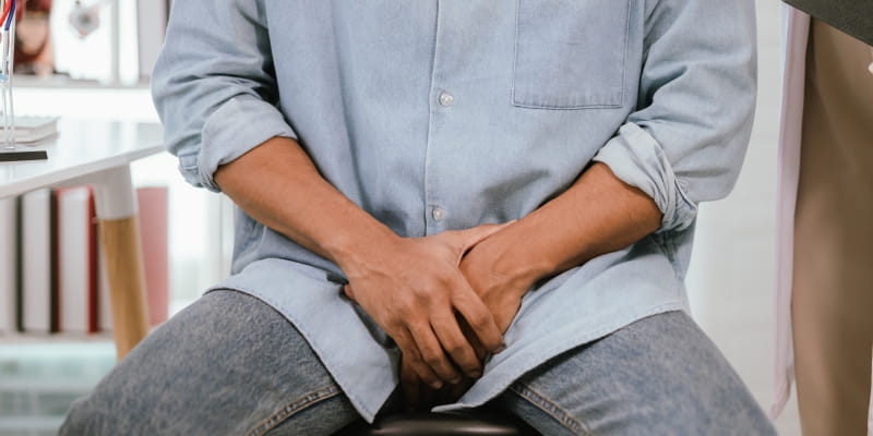 Um homem sentado em uma cadeira, com as mãos nas partes, indicando sinais de alerta na saúde masculina.
