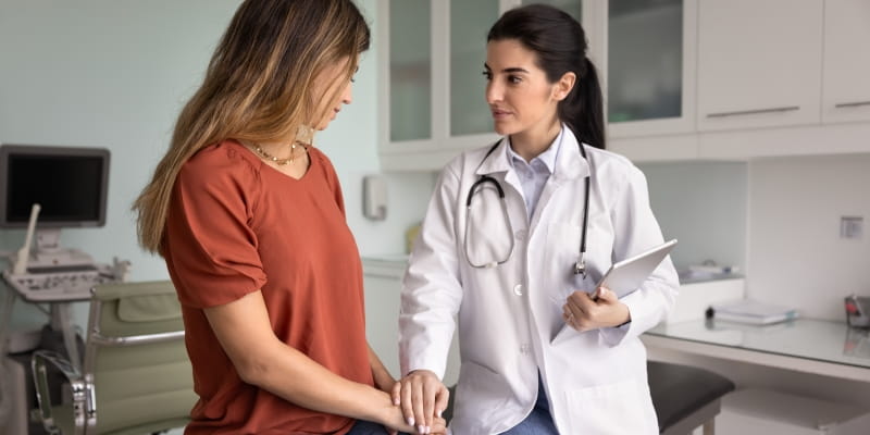 Uma mulher paciente sendo acolhida pela médica após receber um diagnóstico ruim em um consultório, ilustrando o aumento de casos de câncer em jovens.