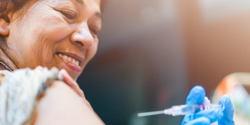 Um mulher, com cerca de 60 anos, sorrindo, feliz, antes de receber a vacina de sarampo.