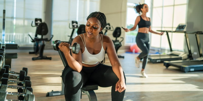 Duas jovens fazendo atividade física em uma academia de musculação, após compreender que envelhecimento saudável começa aos 20 anos.