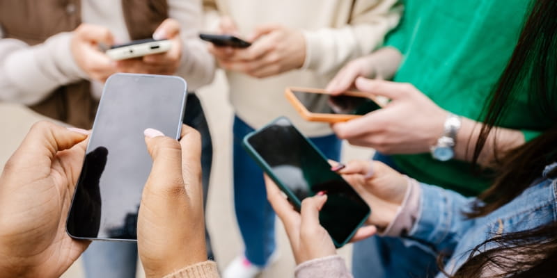 Grupo jovem de pessoas usando telefones celulares e ilustrando o uso excessivo de redes sociais por adolescentes.