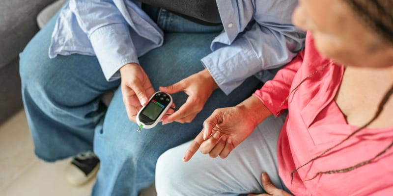 Filha fazendo  teste de glicemia para sua mãe para verificação de diabetes em casa. Imagem para ilustrar a matéria sobre prevenção do diabetes tipo 2.