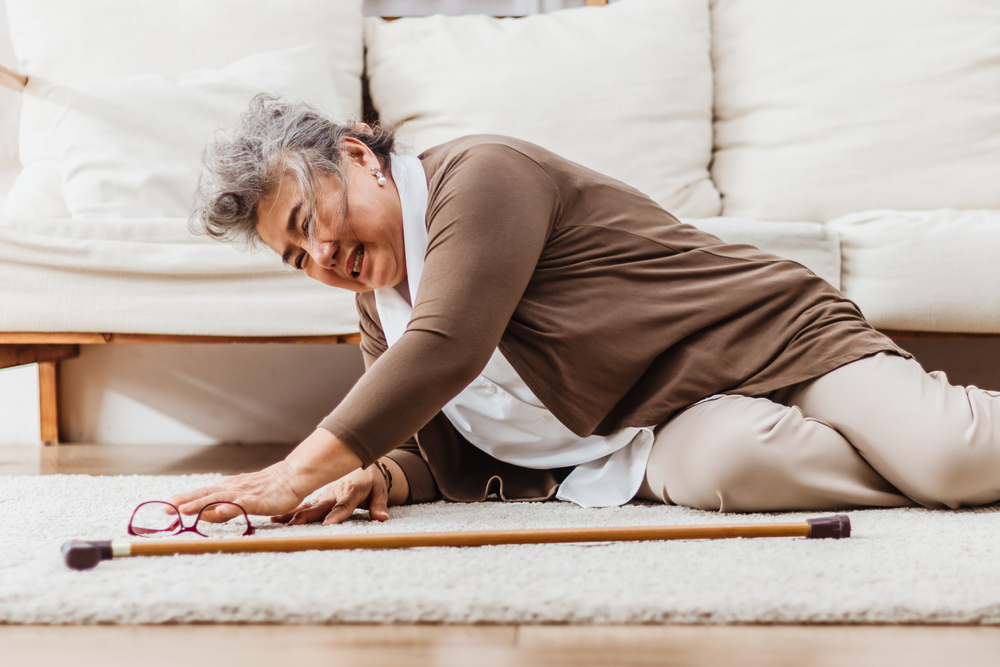 Uma mulher idosa caindo no chão de uma sala, sobre uma tapete. Imagem para ilustrar a matéria sobre acidente doméstico com idosos.