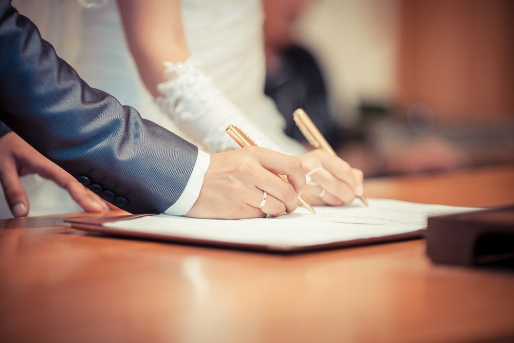Um casal casando e assinando os papéis do casamento. Imagem para ilustrar a matéria sobre relacionamento amoroso e finanças.